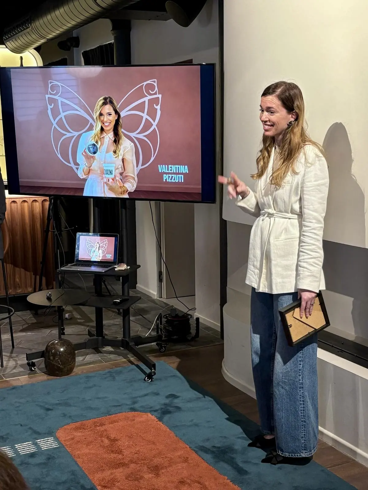 A speaker presents next to a screen showing the event visuals